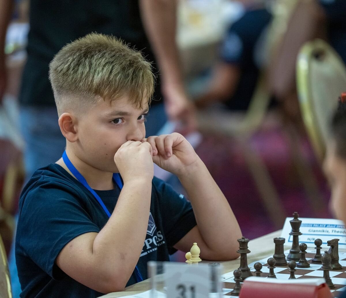 A young chess player thinking with his hands against his face