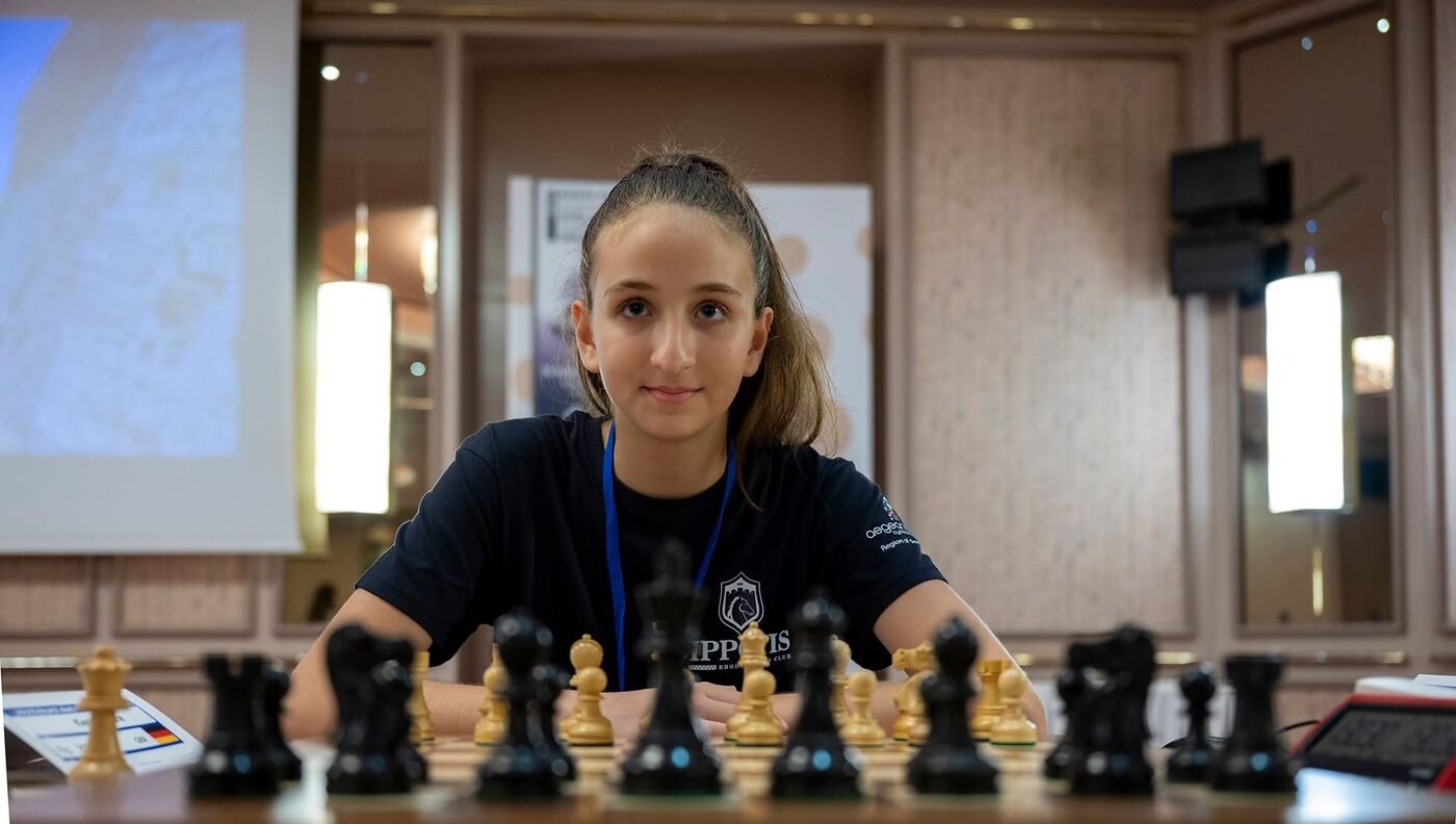An Ippotis player smiles behind the black pieces before her game