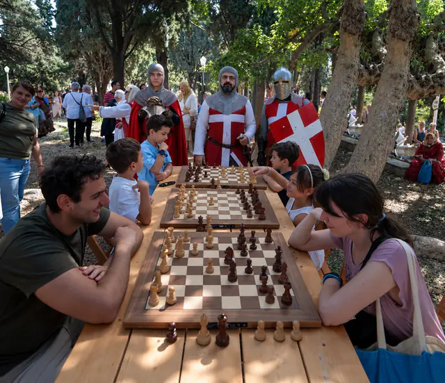 Παιδιά και ενήλικες παίζουν σκάκι στα τραπέζια του Ιππότη, με ιππότες στο βάθος.