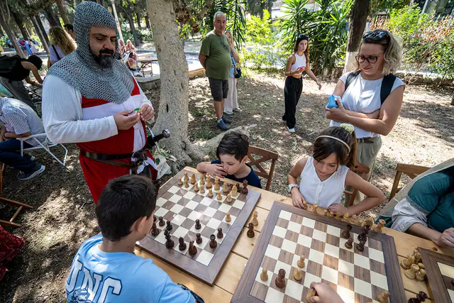 Συμμετέχων με στολή ιππότη δίπλα σε παιδιά που παίζουν σκάκι.