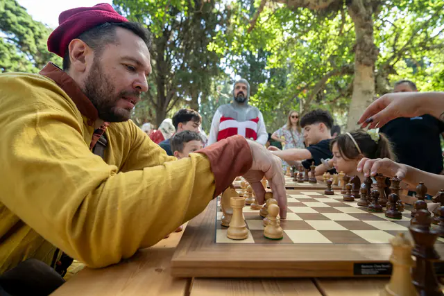Σκακιστής με κίτρινη φορεσιά παίζει μια κίνηση, ενώ συνεχίζονται οι διπλανές παρτίδες.