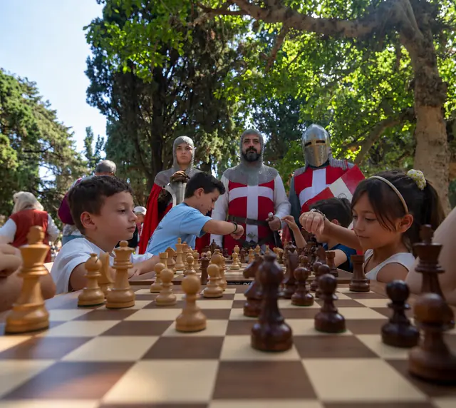 Η σκακιέρα σε πρώτο πλάνο, με παιδιά και ιππότες στο Μεσαιωνικό Φεστιβάλ.