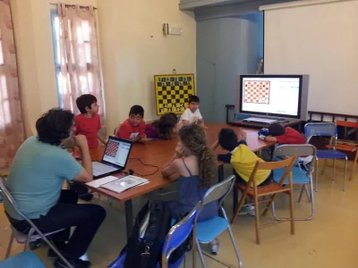 Παιδιά γύρω από το τραπέζι, με σκακιστική θέση στην οθόνη.